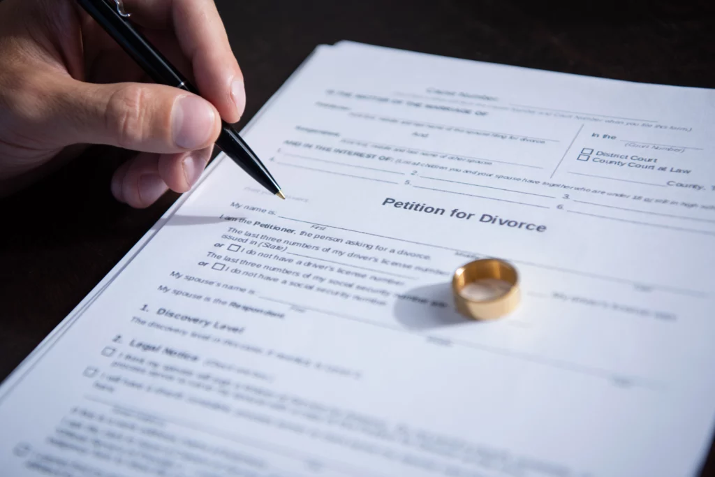 Hand signing a divorce petition with a pen next to a gold wedding ring, symbolizing property division in a California divorce.